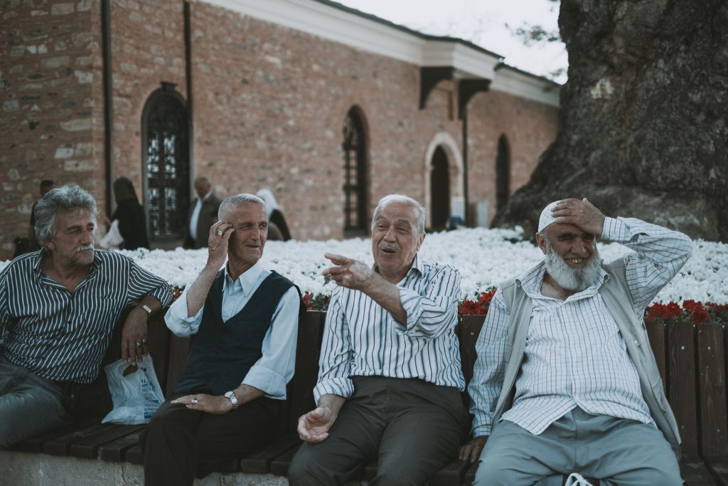 Four elderly men sitting and talking joyfully on a bench outdoors in Bursa, Türkiye.